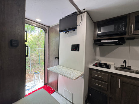 Explore this compact RV rental's interior, featuring a small kitchen with microwave, sink, stovetop, and a fold-down table.