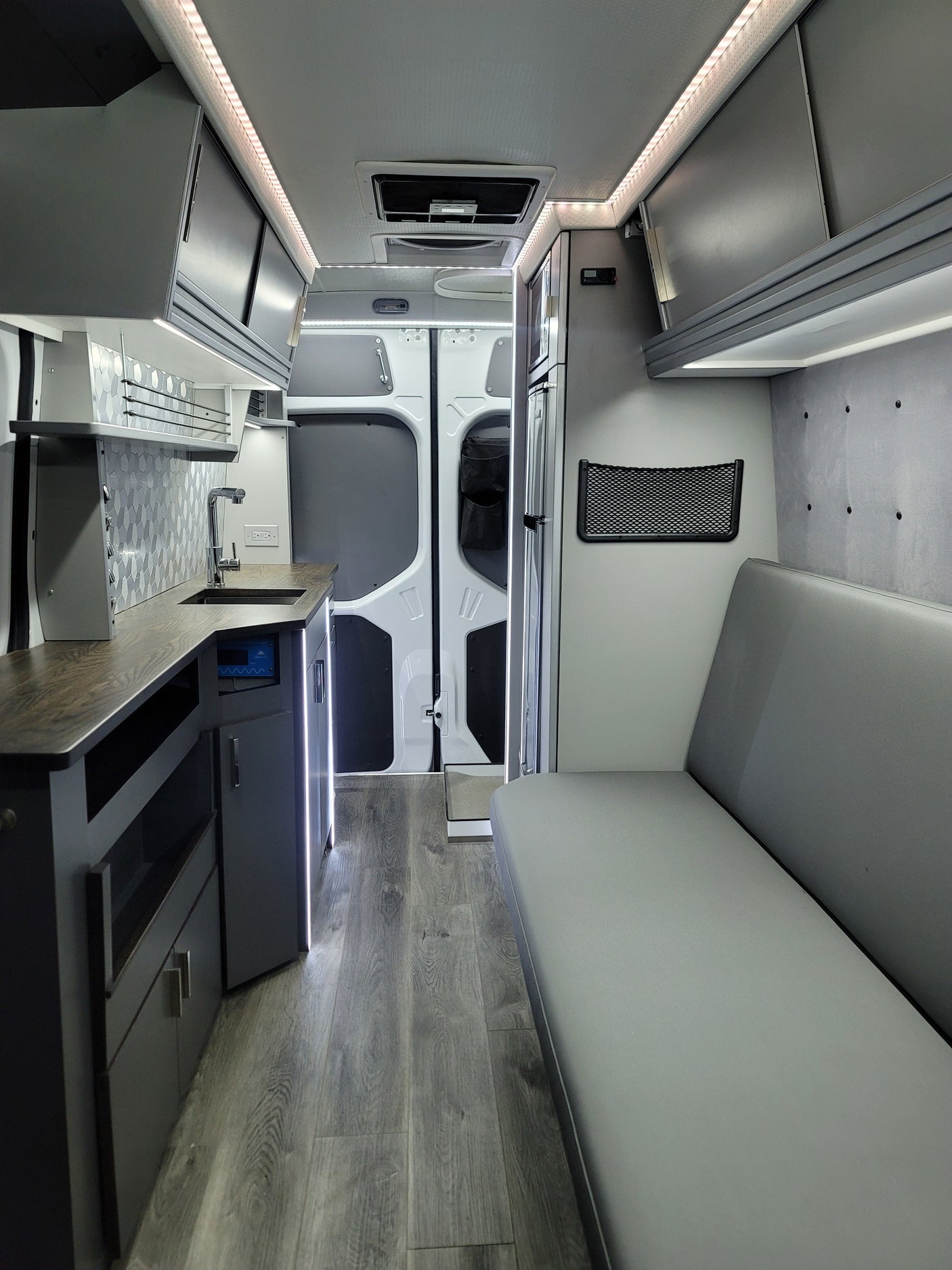 Spacious RV rental interior featuring a modern kitchenette, bright LED lighting, comfortable bench seating, and wood flooring.