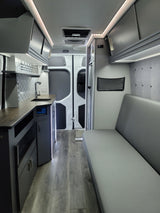 Spacious RV rental interior featuring a modern kitchenette, bright LED lighting, comfortable bench seating, and wood flooring.
