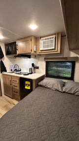 RV rental interior features a compact kitchen with microwave, sink, and fridge, plus a cozy bed for comfortable travel.