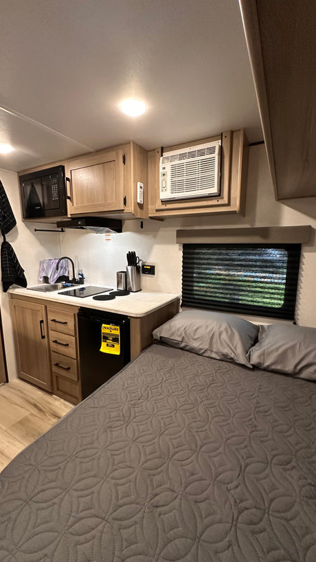 RV rental interior features a compact kitchen with microwave, sink, and fridge, plus a cozy bed for comfortable travel.