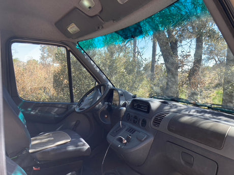 A spacious RV rental van cockpit. Features driver's seat, dashboard, & natural scenery visible through large windows.