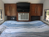 Cozy RV rental bedroom with striped bedding, built-in cabinets, TV, and AC unit for comfortable stays.