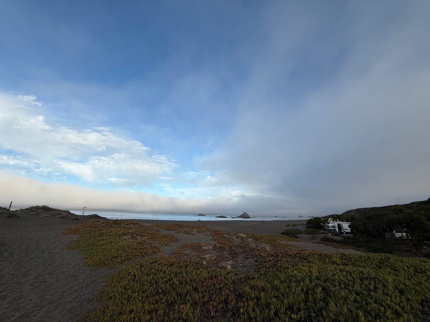 RV rental parked near a misty beach with dense fog rolling in from the ocean.