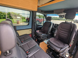 RV rental interior: View from inside a custom van, featuring black seats, wooden cabinets, and a scenic outdoor view.