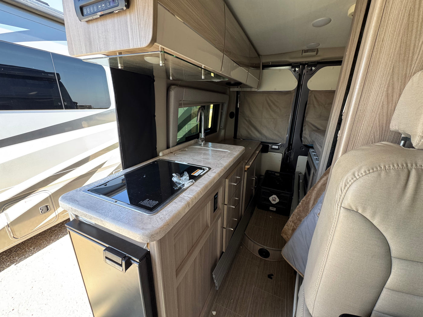 Modern RV rental interior: kitchen with induction stovetop, sink, fridge, and cabinets. Cozy, compact living space. — photo 6