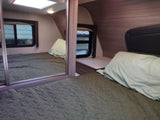 Comfortable RV rental bedroom with a mirrored closet, quilted bed, and bedside table, offering cozy accommodations.