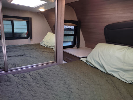 Comfortable RV rental bedroom with a mirrored closet, quilted bed, and bedside table, offering cozy accommodations.