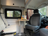 RV rental interior featuring a table with chips, cheese, and sour cream. Cozy seats and forest views outside.