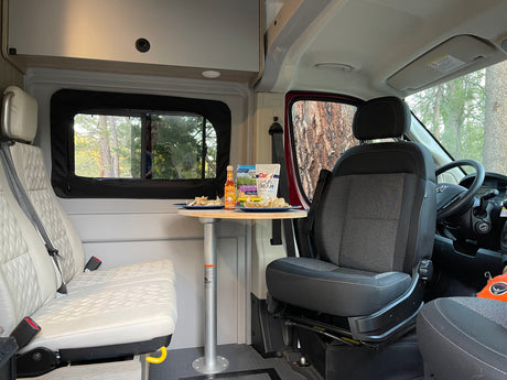RV rental interior featuring a table with chips, cheese, and sour cream. Cozy seats and forest views outside.