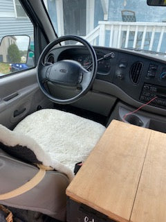 Inside an RV rental van: The driver's seat, dashboard, and steering wheel are visible, featuring a soft seat cover.