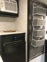 An RV rental interior features an AC unit, compact kitchenette with fridge, and a door with a grey hanging organizer.