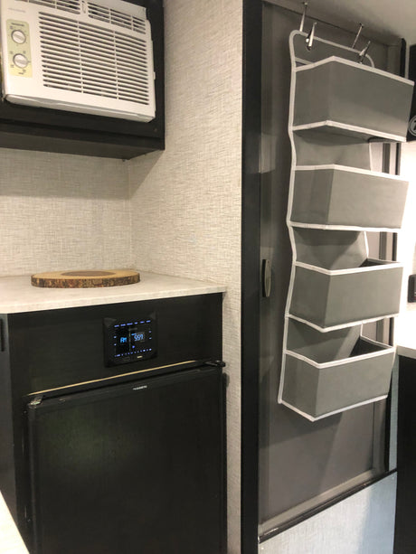 An RV rental interior features an AC unit, compact kitchenette with fridge, and a door with a grey hanging organizer.
