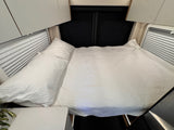 Overhead view of a cozy RV rental bed with white quilted bedding, pillows, and window blinds.