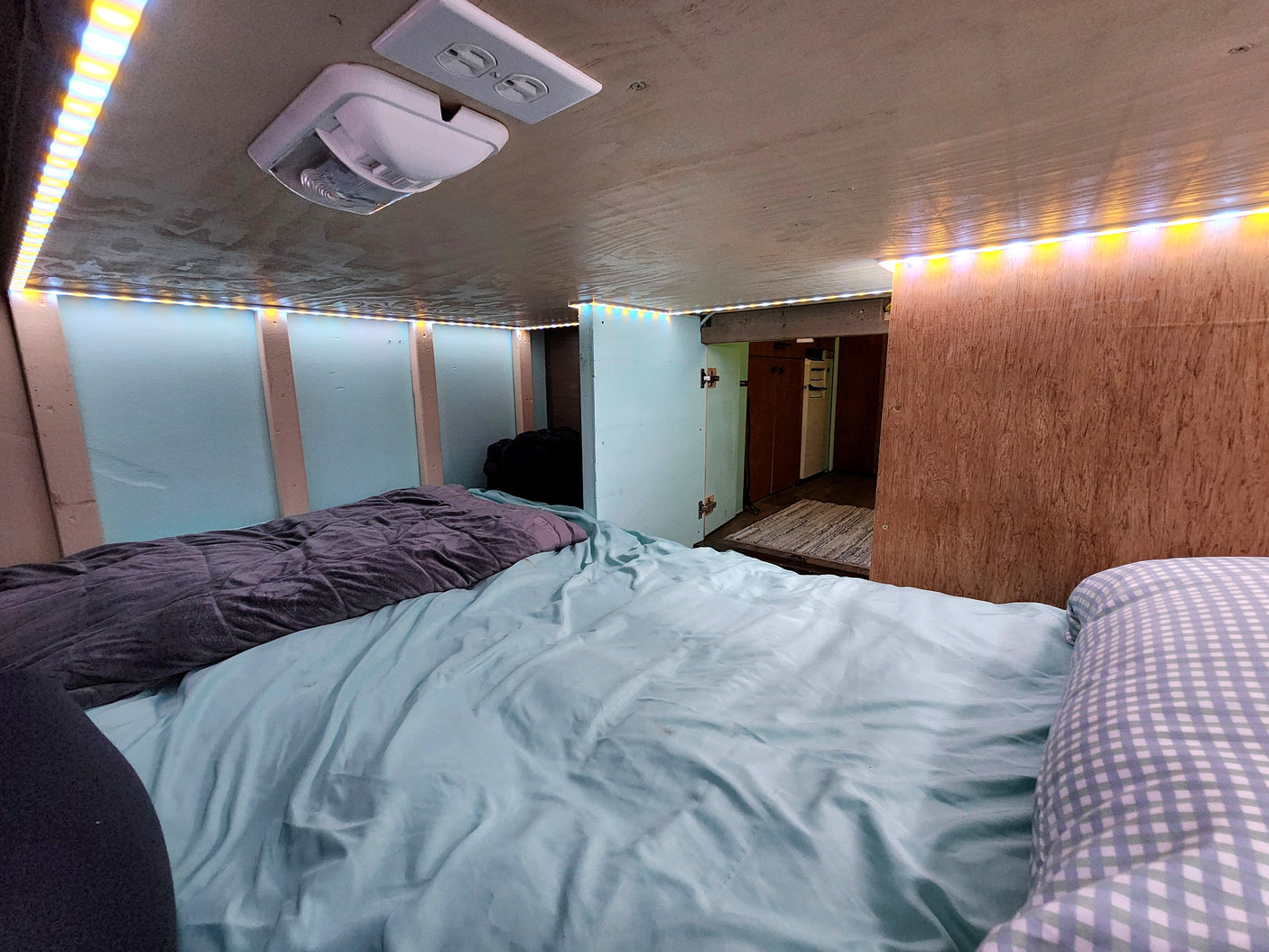 Cozy RV rental interior with a bed, warm LED strip lights overhead, and functional amenities for compact living.
