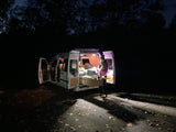 Night setup in an RV rental van: A person prepares food at a pull-out kitchen under ambient lights.