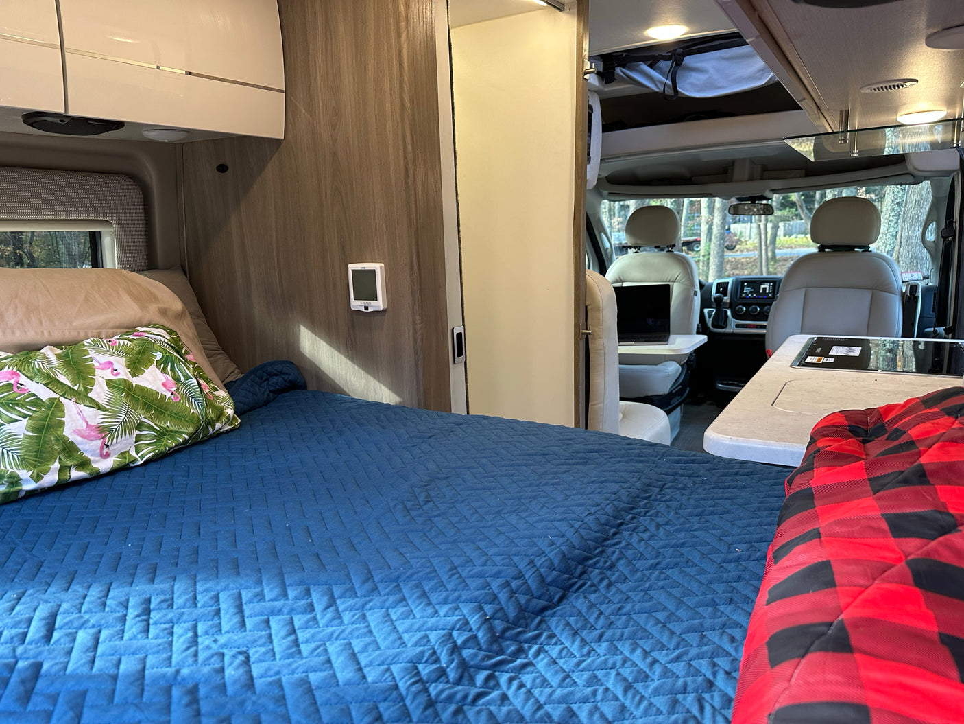 Inside a spacious RV rental: a plush bed with a flamingo pillow, functional kitchen, and front cockpit. Ready for travel!