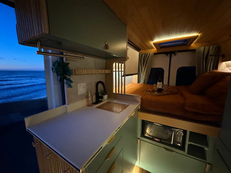 Cozy rv rental interior featuring a kitchen, microwave, comfy bed, and a serene ocean view from the window.