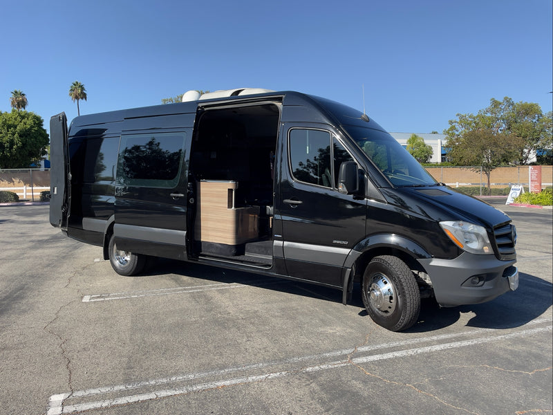 Black Sprinter RV rental, with side and rear doors open, showcases its customized camper interior in a sunny lot. — photo 16