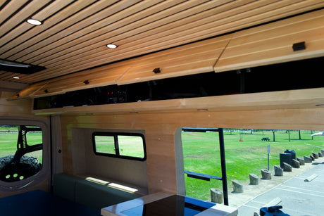 Experience this RV rental's cozy wood interior, featuring overhead storage, comfortable seating, and scenic park views through large windows.