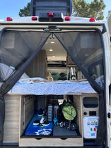 Inside this rv rental: rear view reveals a bed over storage containing a wakeboard, golf clubs, luggage, and utility panel.