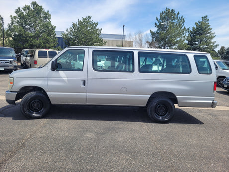 Side view of a silver multi-passenger van, seen in a parking lot. This type is often used for group travel or as an RV rental.