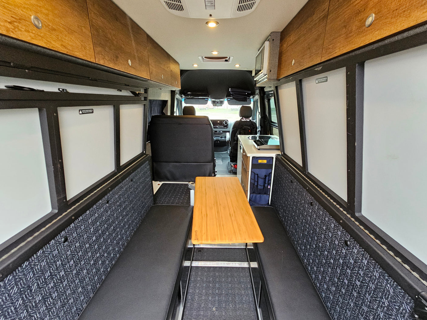 Inviting RV rental interior showcasing a cozy dining area, kitchenette, and overhead storage in a modern camper van.