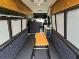 Inviting RV rental interior showcasing a cozy dining area, kitchenette, and overhead storage in a modern camper van.