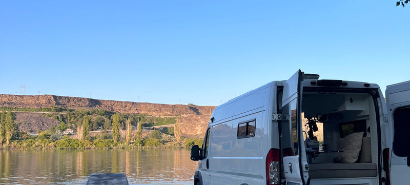 This RV rental offers stunning waterside views. Open doors reveal a cozy camper van interior by cliffs & clear skies. Ideal for travel. — photo 5