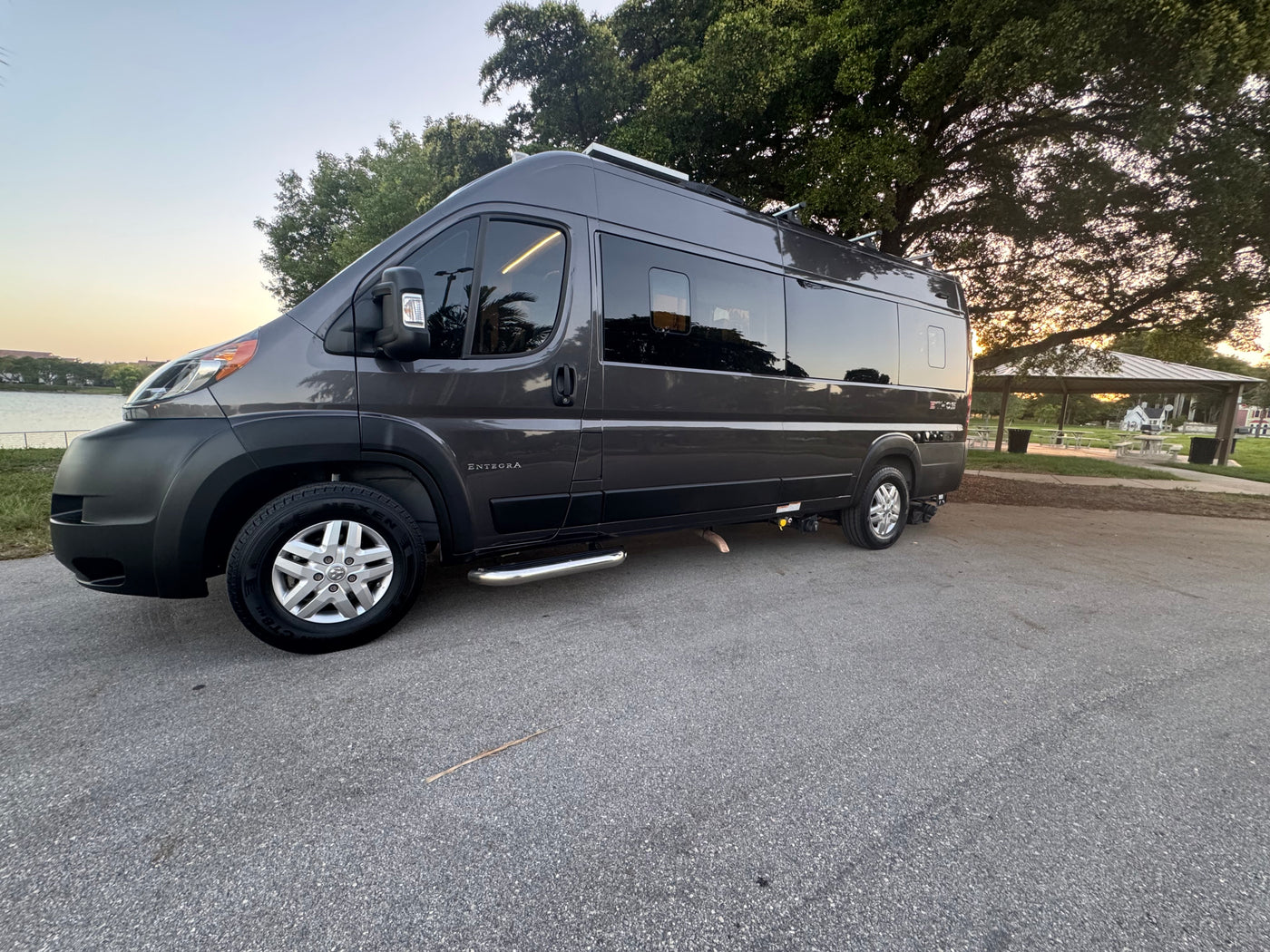 This sleek gray camper van, ideal for RV rental travel, is parked by a scenic lake with trees under a clear sky. — photo 11
