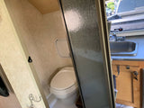 Inside an RV rental: a compact bathroom with a toilet, partially visible through a textured shower door, next to a functional sink.