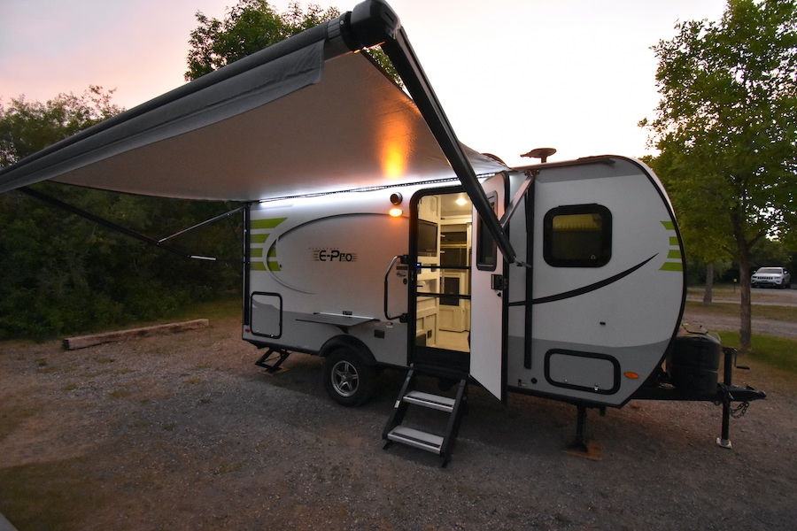 This E-Pro travel trailer (rv rental) is illuminated at dusk in a campsite, with its awning extended and door open, ready for camping. — photo 10