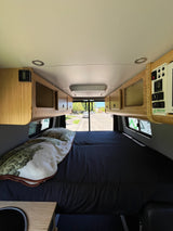 Inside an RV rental adventure van, featuring a comfy bed, bamboo overhead cabinets, and detailed control panel.