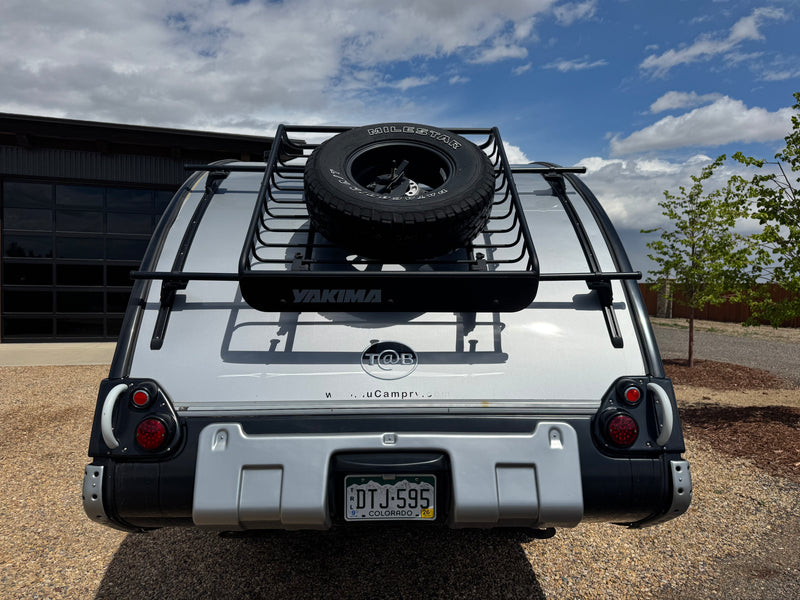 Rear view of a T@B teardrop RV rental, featuring a silver exterior, a Yakima roof rack, and a mounted spare tire, ready for camping. — photo 8