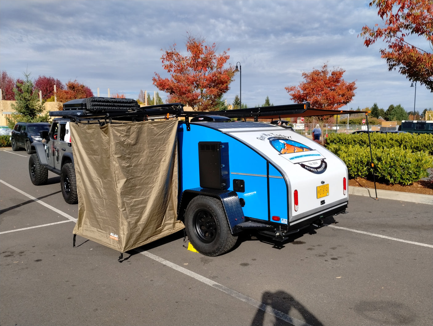 An RV rental teardrop trailer, with a privacy tent & solar panels, towed by a Jeep Wrangler.