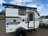A white and grey Sunray Sport teardrop RV trailer, ideal for rv rental adventures, parked outdoors with an awning.