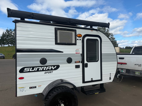 A white and grey Sunray Sport teardrop RV trailer, ideal for rv rental adventures, parked outdoors with an awning.