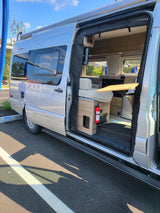 Explore this sleek silver RV rental! The open side door reveals a well-equipped interior with seating & a table.