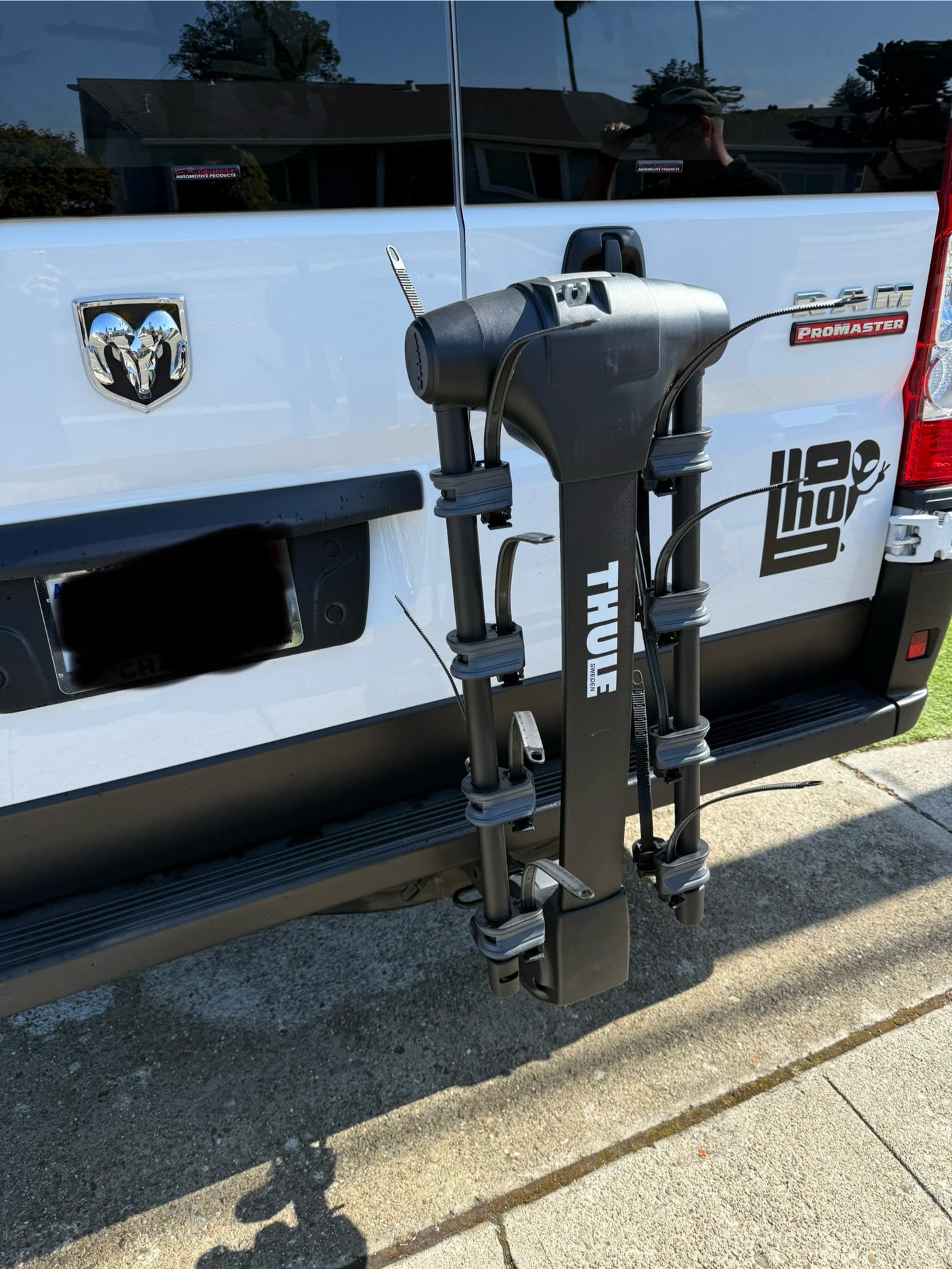 Rear view of a white Ram ProMaster rv rental van with a black Thule bike rack attached to the hitch.