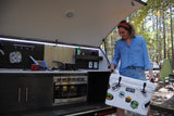 This RV rental features an outdoor kitchen. A woman loads a cooler adorned with National Park stickers, ready for campsite cooking.