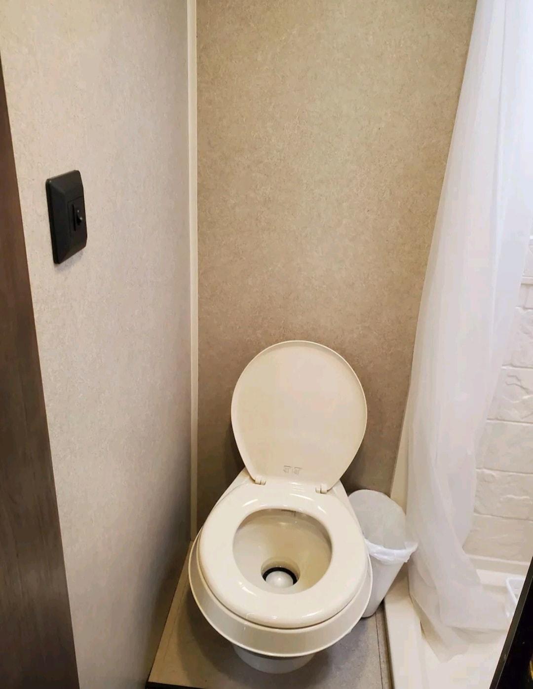 Compact RV rental bathroom features a white toilet with an open lid, adjacent shower curtain, and wall light switch. — photo 5