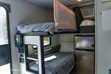 RV rental interior featuring cozy bunk beds with a child safety rail, a compact fridge, & controls. Compact living space.