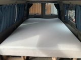 This spacious rv rental conversion features a large white mattress on a sturdy wooden bed frame inside the van, creating a comfortable sleeping area.
