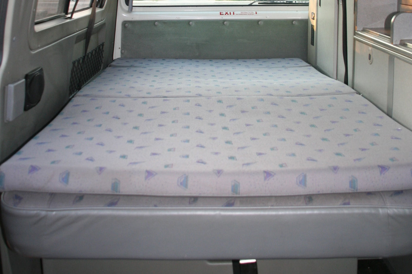 RV rental interior featuring a neatly made bed with patterned cushions on a grey base, ideal for compact travel. — photo 5