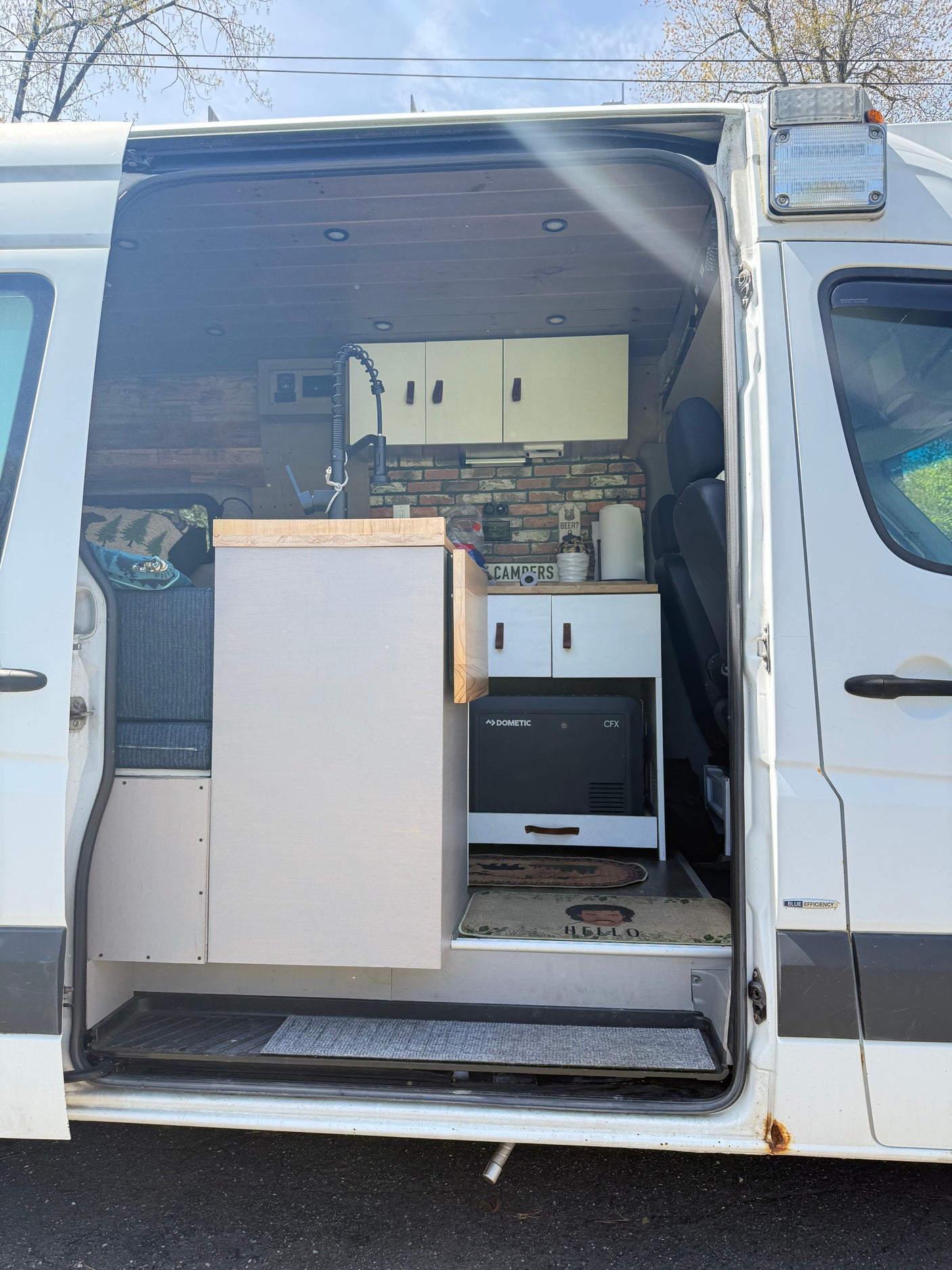 Open side door of an RV rental showing a camper van interior with kitchen, Dometic fridge, seating, and overhead lights.