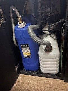 RV rental: Portable water tanks under counter. Blue Igloo and white jugs with hoses provide mobile water.