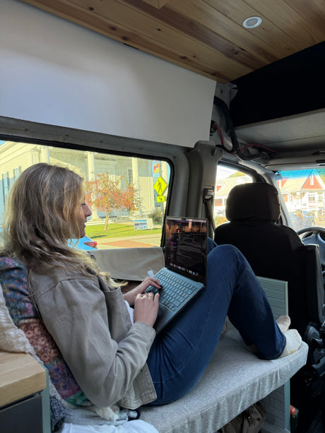 A woman works on her laptop inside an RV rental, showcasing remote work on the go with a street view outside.