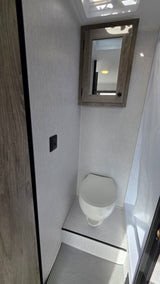 RV rental interior: compact bathroom featuring a clean toilet, mirrored cabinet, and shower area with light walls.