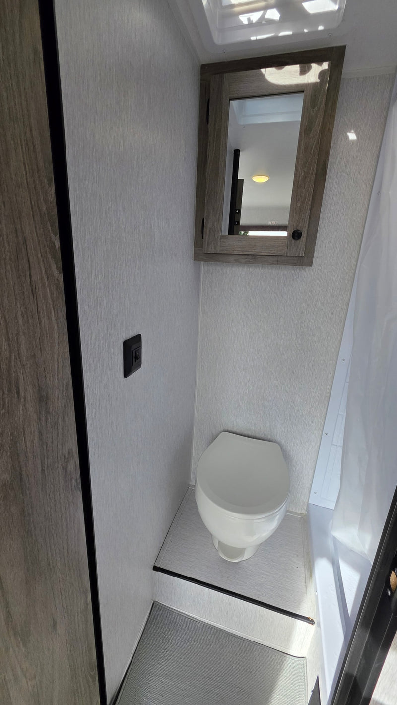 RV rental interior: compact bathroom featuring a clean toilet, mirrored cabinet, and shower area with light walls. — photo 12