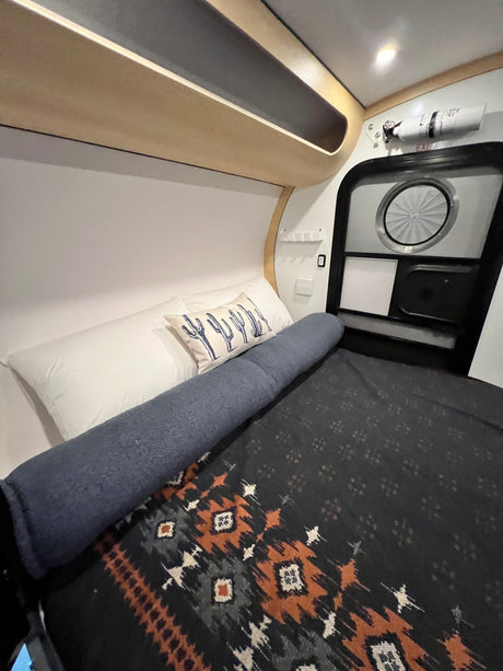 Step inside this cozy RV rental's sleeping area, featuring a Southwestern blanket, cactus pillow, and compact design.